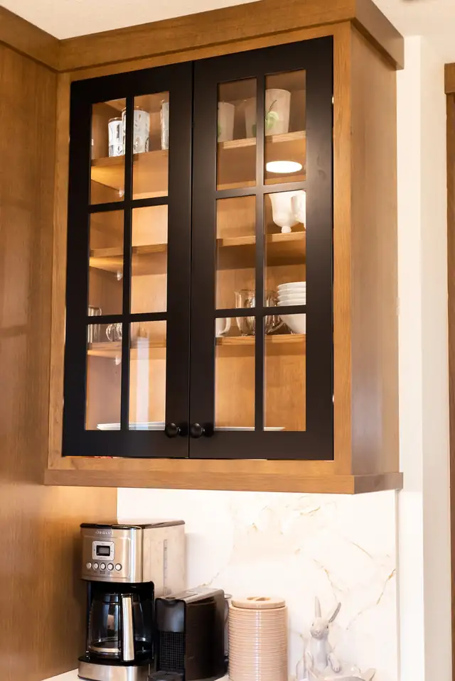 Black-framed glass-front upper cabinet over a coffee station with marble-look quartz backsplash