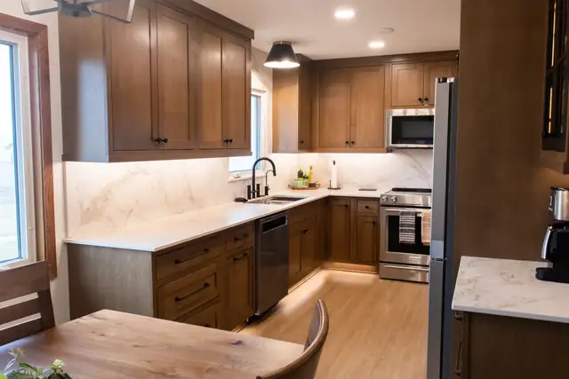 U-shaped kitchen with warm wood cabinets, under-cabinet lighting and marble-look quartz counters seen from the dining table
