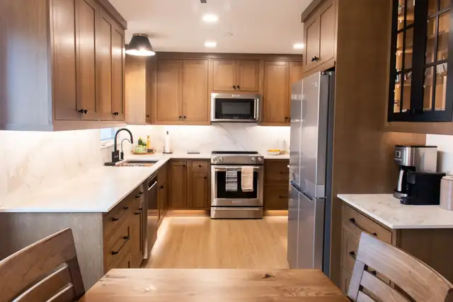 Galley kitchen with stained shaker cabinets, full-height marble-look quartz backsplash and light vinyl plank floor