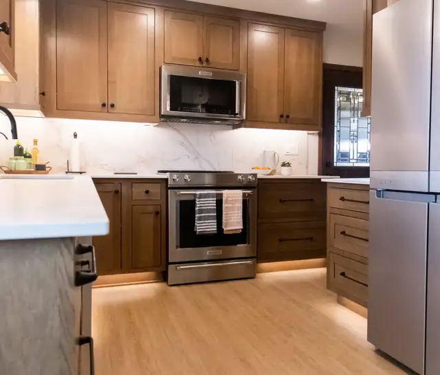 Kitchen remodel with warm stained shaker cabinets, marble-look quartz backsplash, stainless range and under-cabinet lighting