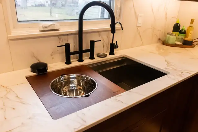 Marble-look quartz countertop with black workstation sink, cutting board insert and matte black bridge faucet
