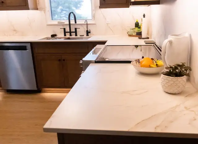 Kitchen by Completely Kitchens with stained wood cabinets, a white marble-look quartz counter and full-height backsplash, a black faucet and under-cabinet lighting