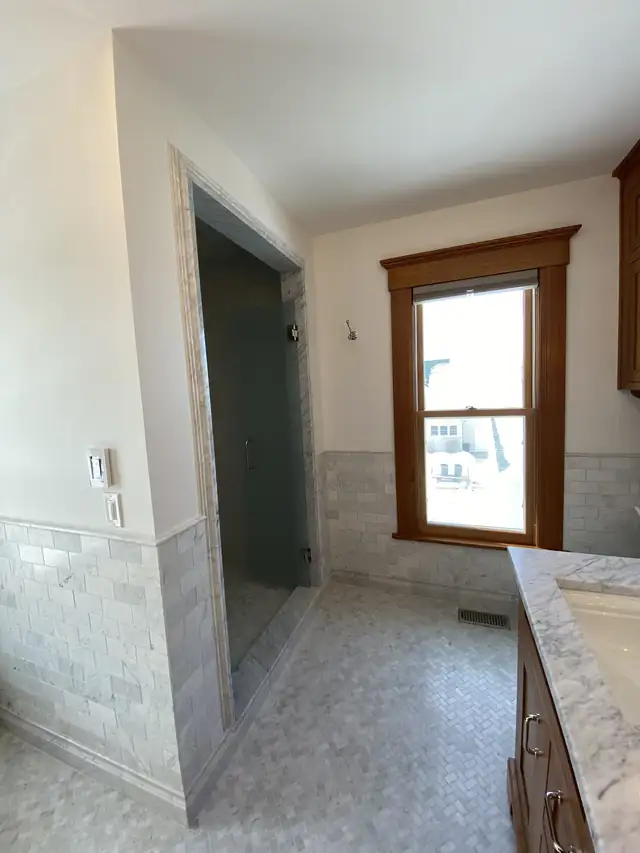 Bathroom remodel near Ames, Iowa with tiled walk-in shower, marble wainscot and stained wood window trim