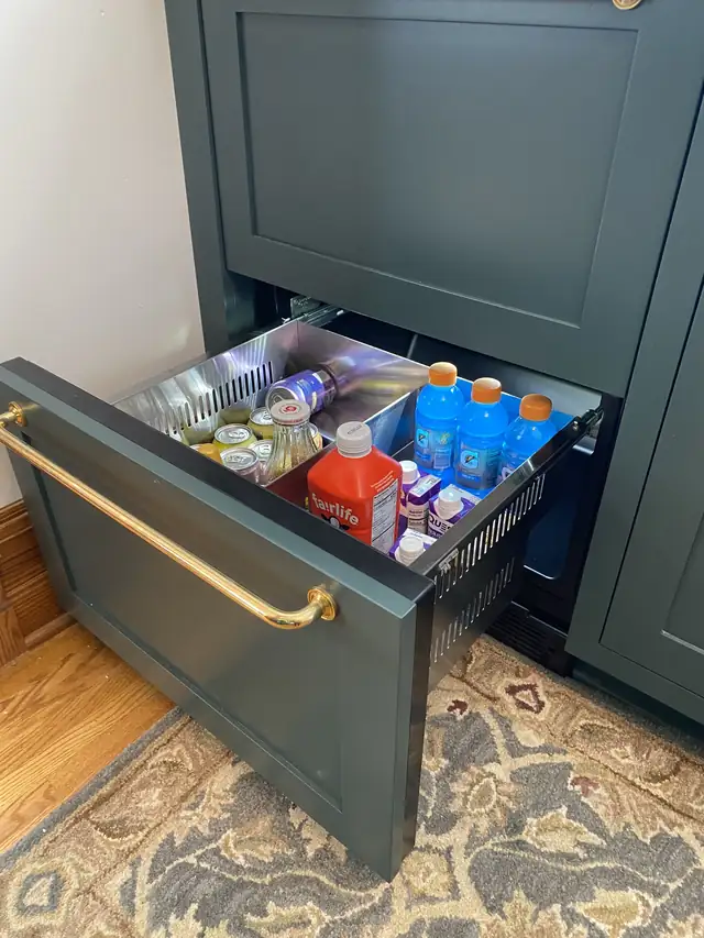 Panel-ready beverage fridge drawer in a deep green cabinet with brass pull