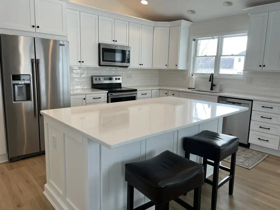 Kitchen remodeling Ames, Iowa project by Completely Kitchens: white shaker cabinets, white island with quartz top and black stools, subway tile backsplash