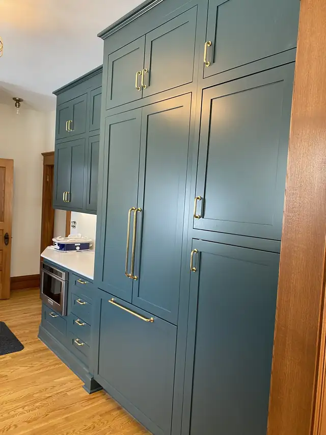 Deep green full-height cabinets with brass pulls beside a wood-trimmed doorway